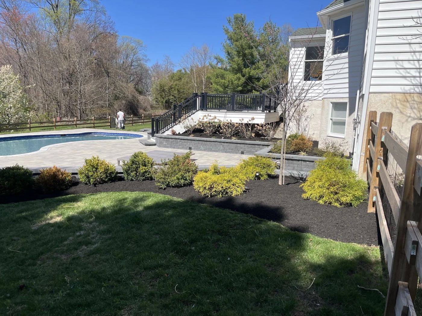 Poolside landscaping with fresh mulch, shrubs, stone walls and a paved terrace